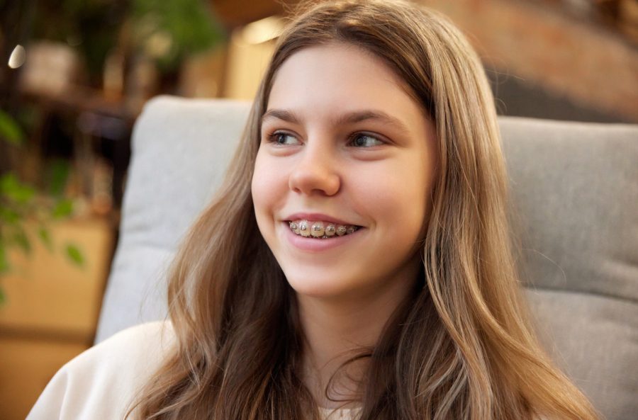 orthodontics Close up portrait of young attractive girl smiling with teeth in braces sitting in arm chair and looking away. Concept of youth, health care, perfect smile, dental problems.